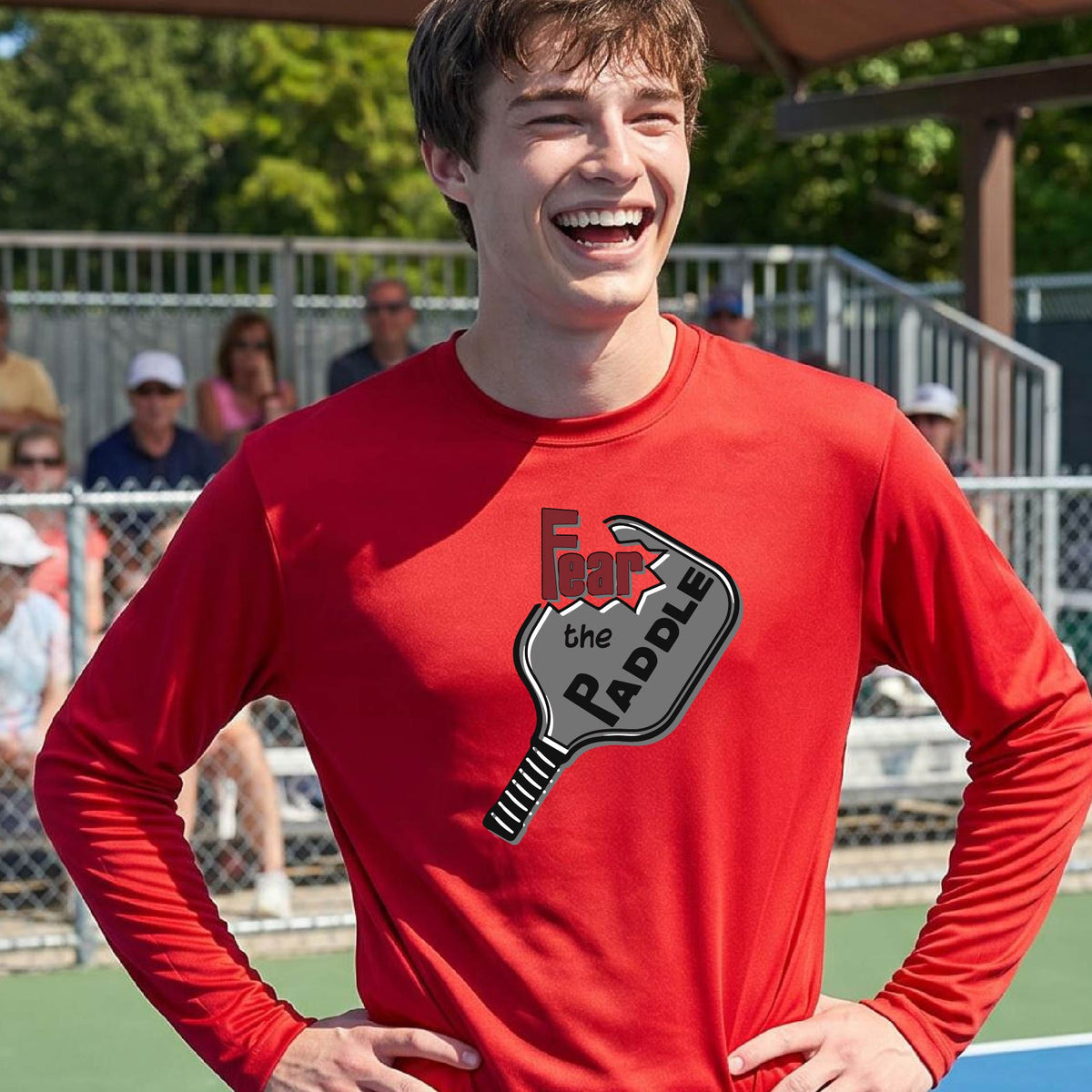 A man wearing a long-sleeve red shirt with a pickleball graphic of the words 'FEAR THE PADDLE' cut into a pickleball paddle. 