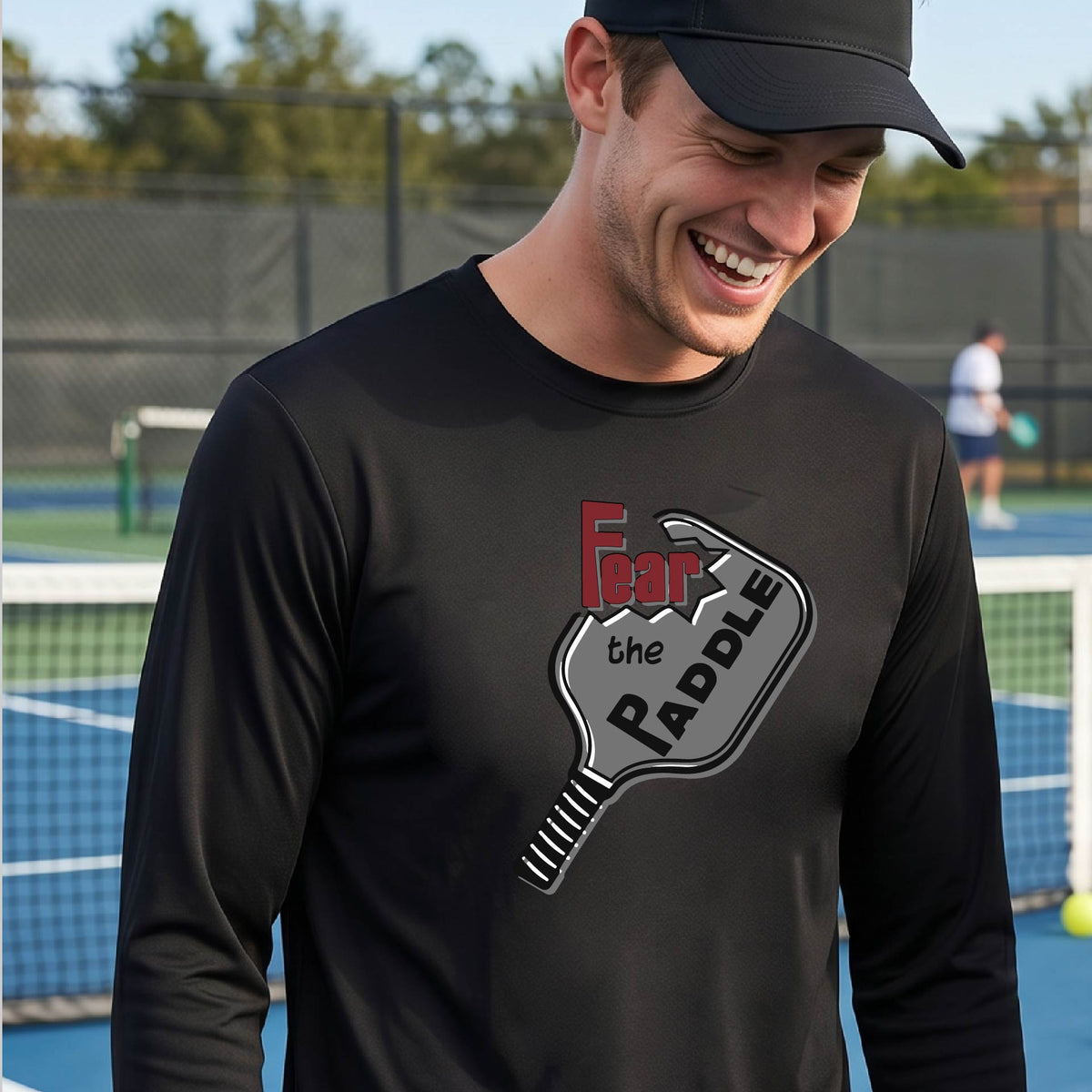 A man wearing a long-sleeve black shirt with a pickleball graphic of the words 'FEAR THE PADDLE' cut into a pickleball paddle. 