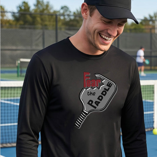 A man wearing a long-sleeve black shirt with a pickleball graphic of the words 'FEAR THE PADDLE' cut into a pickleball paddle. 
