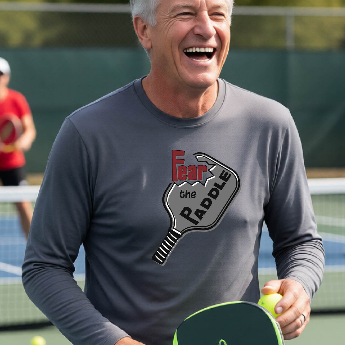 A man wearing a long-sleeve grey shirt with a pickleball graphic of the words 'FEAR THE PADDLE' cut into a pickleball paddle. 