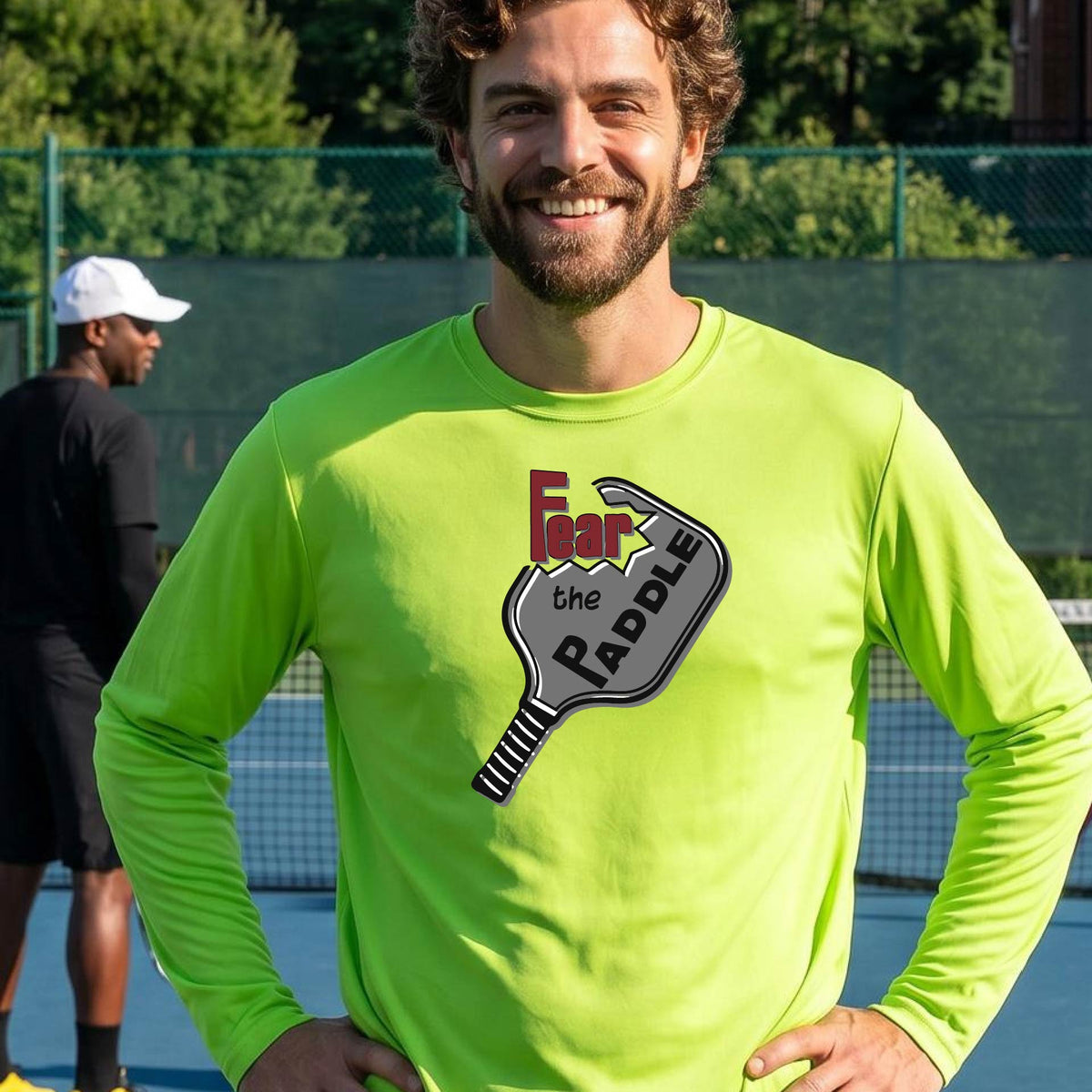 A man wearing a long-sleeve lime green shirt with a pickleball graphic of the words 'FEAR THE PADDLE' cut into a pickleball paddle. 