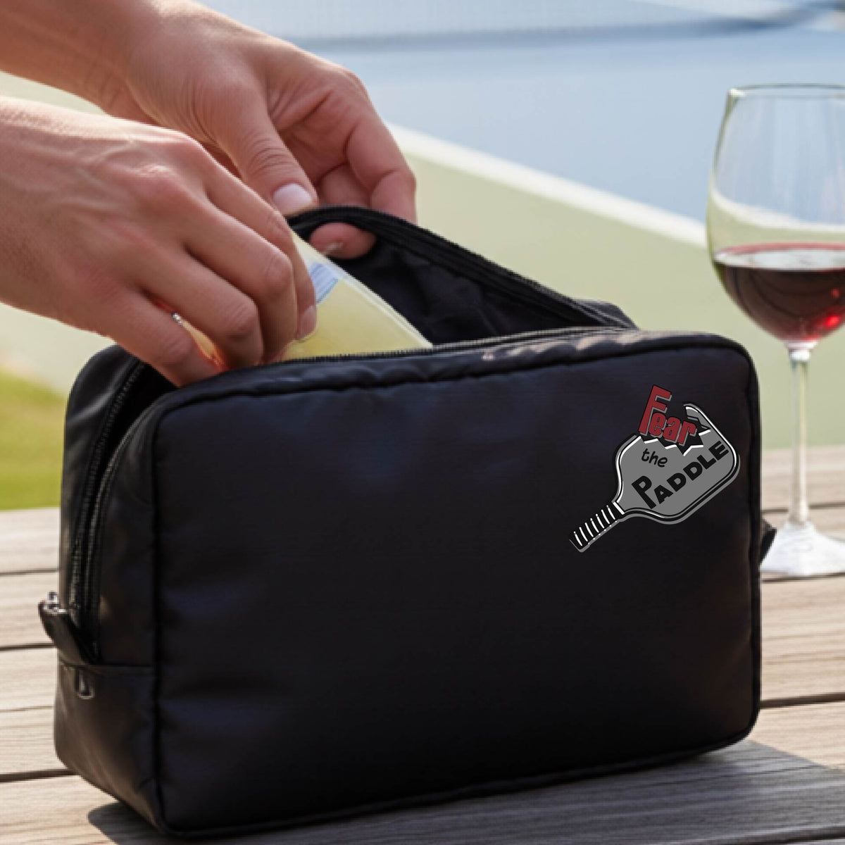 A black cosmetic bag with a zippered closure and a pickleball graphic of the text 'FEAR THE PADDLE' with the words cut into a pickleball paddle. 