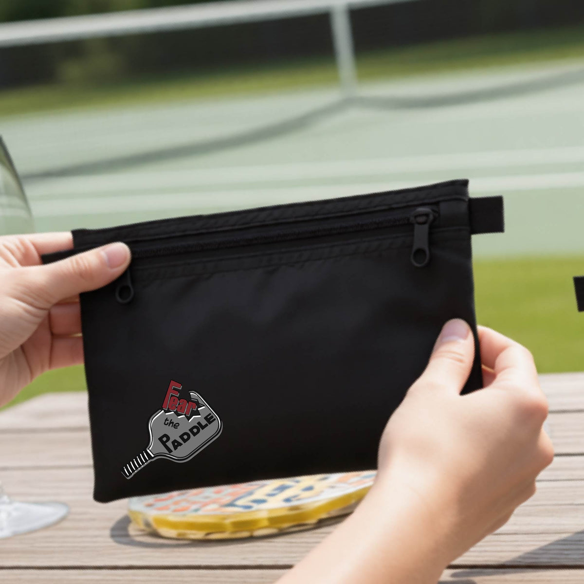 A black cosmetic bag with a pickleball graphic of the text 'FEAR THE PADDLE' cut into a pickleball paddle. 