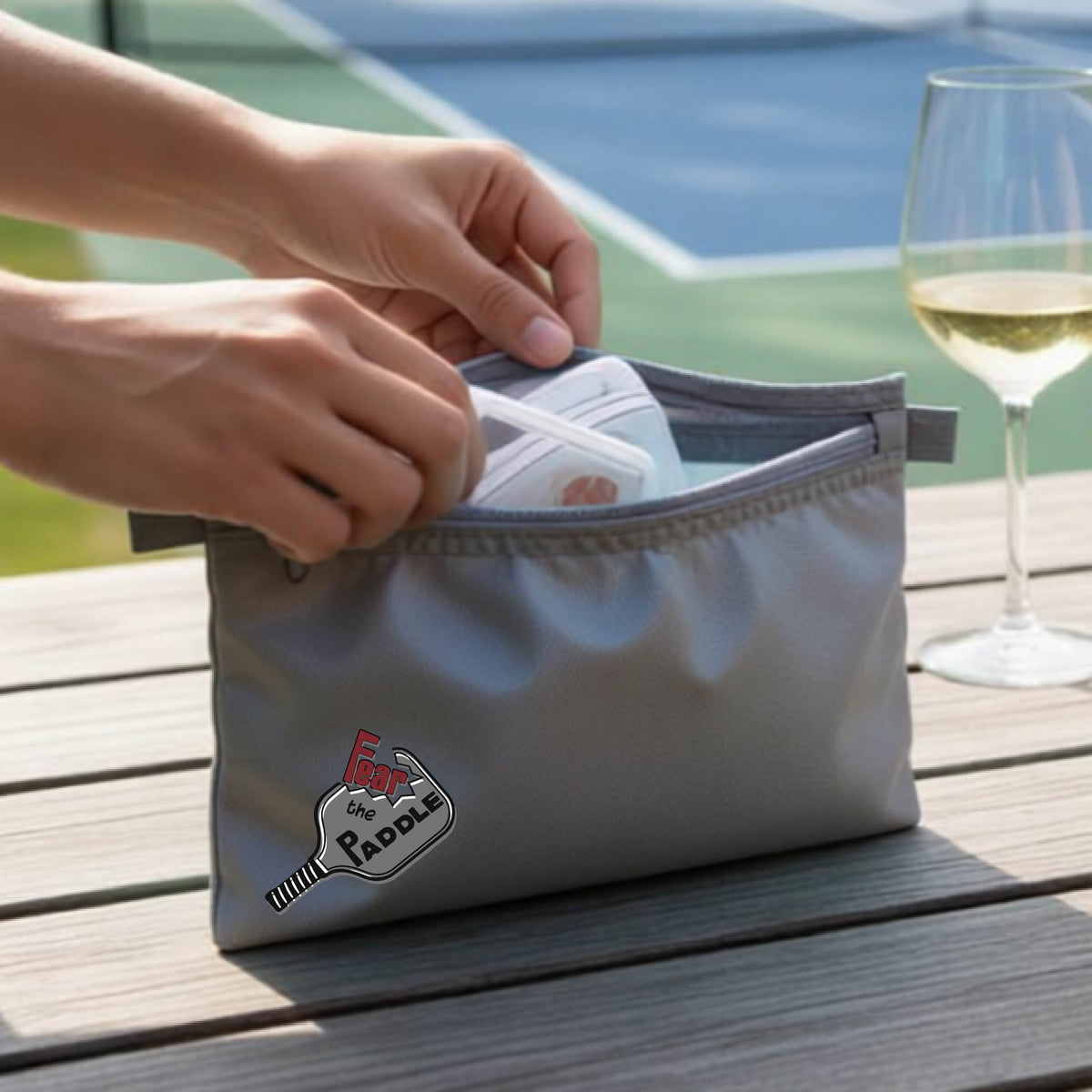 A gray cosmetic bag with a pickleball graphic of the text 'FEAR THE PADDLE' cut into a pickleball paddle. 