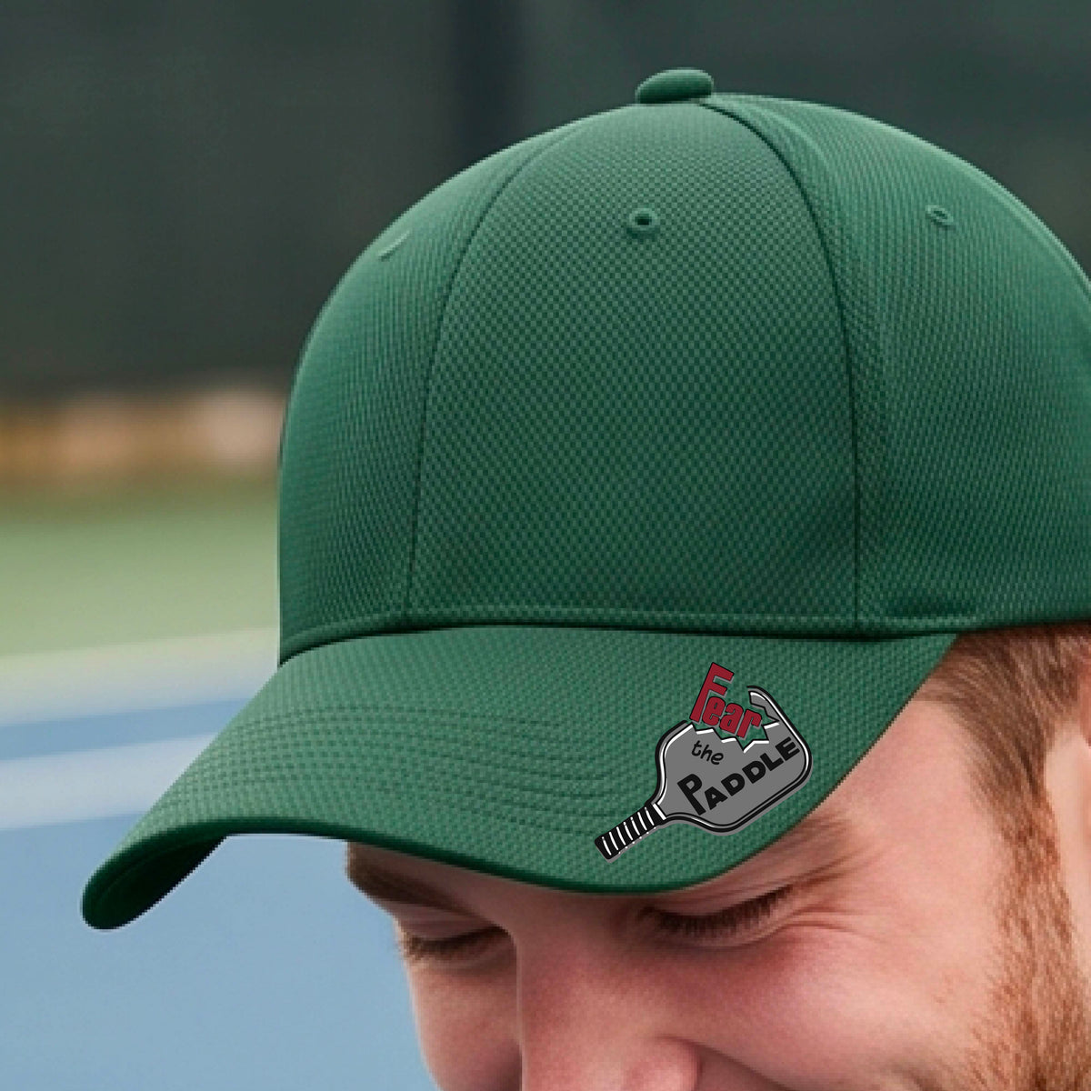 A close up of a green baseball cap with a black paddle-shaped logo that reads 'Fear the Paddle' and a pickleball paddle graphic. 