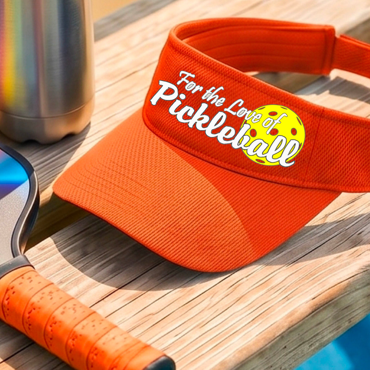 A close-up of an orange pickleball visor with a pickleball graphic of ‘FOR THE LOVE OF PICKLEBALL’ in white with a yellow pickleball behind it graphic on the front.