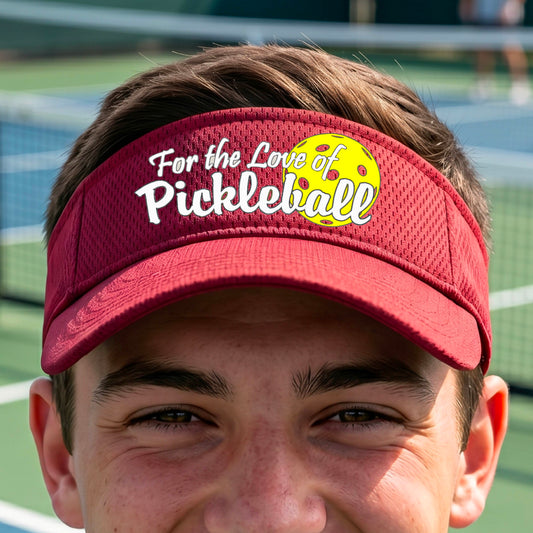 A close-up of a red pickleball visor with a pickleball graphic of ‘FOR THE LOVE OF PICKLEBALL’ in white with a yellow pickleball behind it graphic on the front.