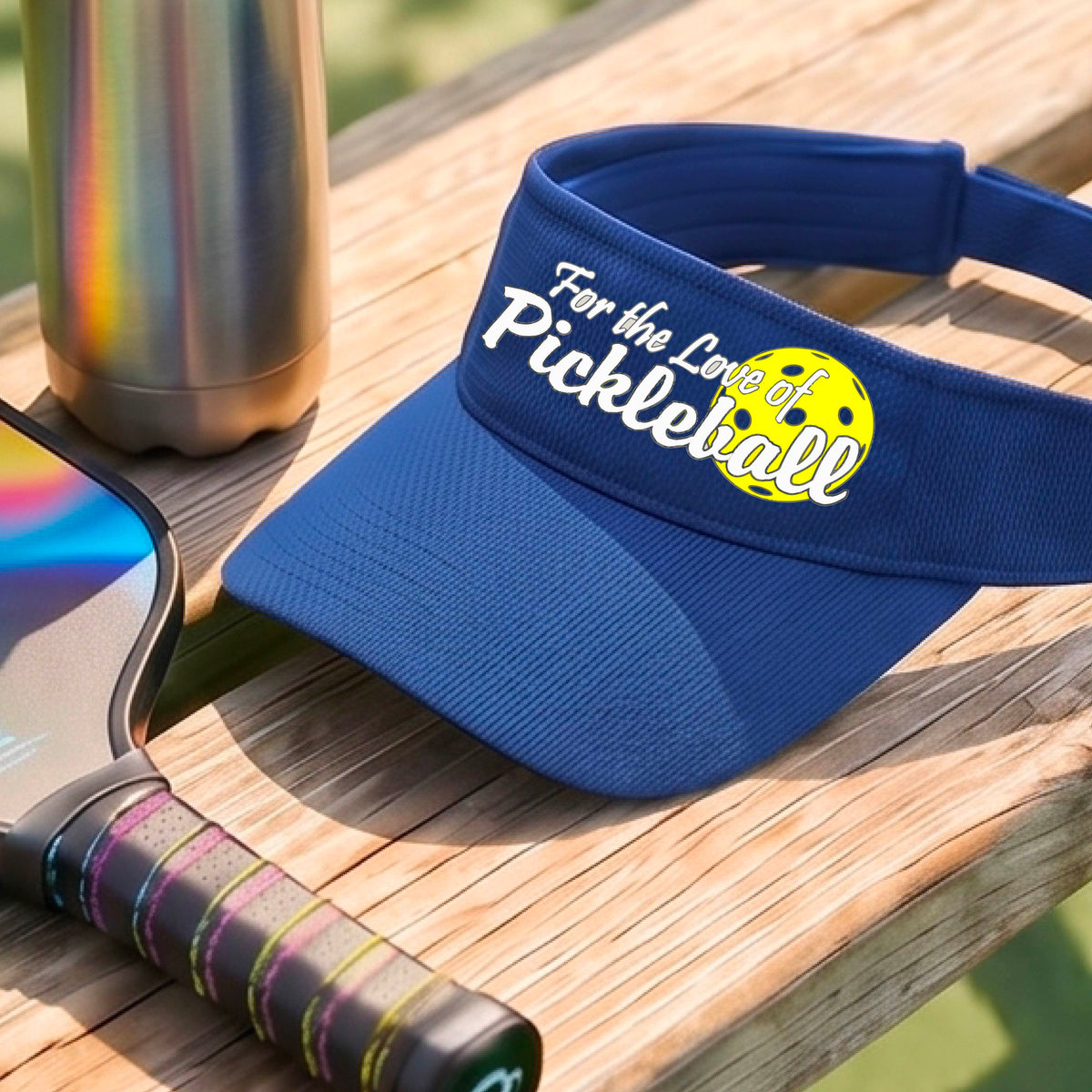 A close-up of a royal blue pickleball visor with a pickleball graphic of ‘FOR THE LOVE OF PICKLEBALL’ in white with a yellow pickleball behind it graphic on the front.