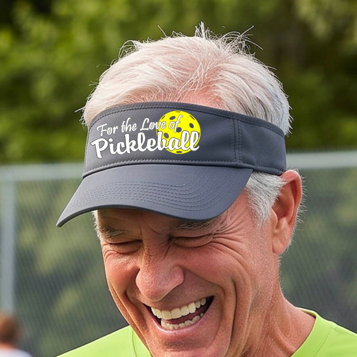 A close-up of a gray pickleball visor with a pickleball graphic of ‘FOR THE LOVE OF PICKLEBALL’ in white with a yellow pickleball behind it graphic on the front.