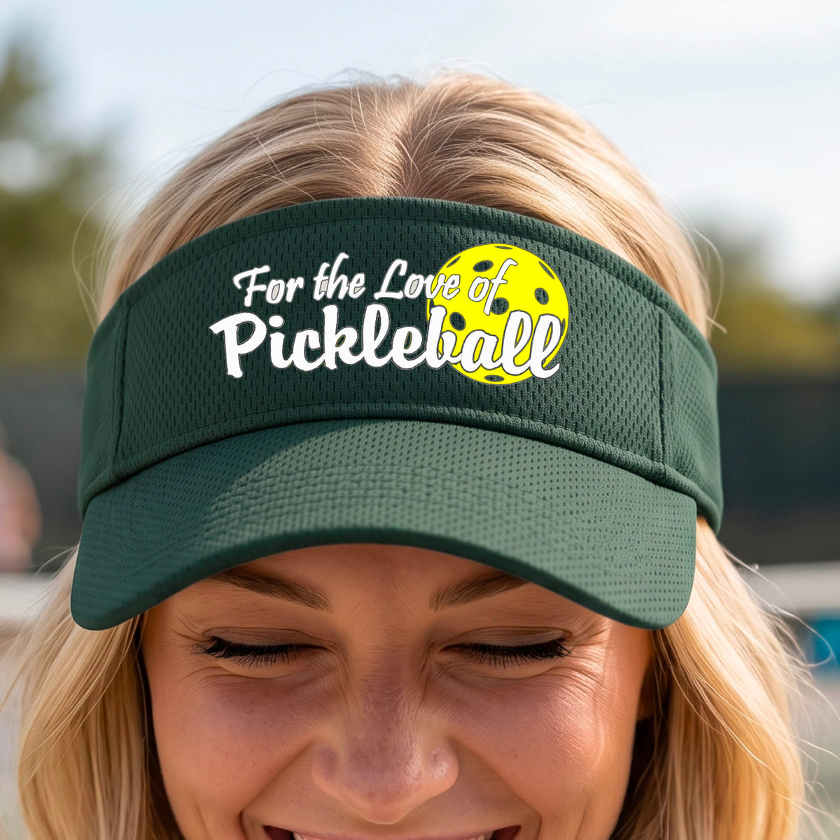 A close-up of a green pickleball visor with a pickleball graphic of ‘FOR THE LOVE OF PICKLEBALL’ in white with a yellow pickleball behind it graphic on the front.