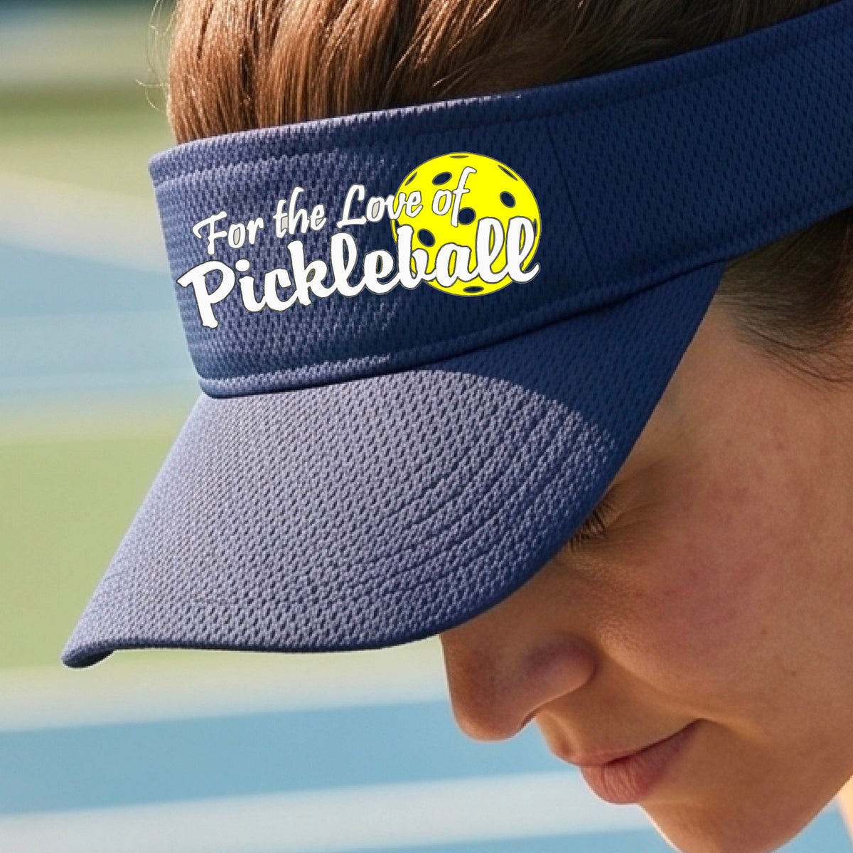 A close-up of a navy blue pickleball visor with a pickleball graphic of ‘FOR THE LOVE OF PICKLEBALL’ in white with a yellow pickleball behind it graphic on the front.