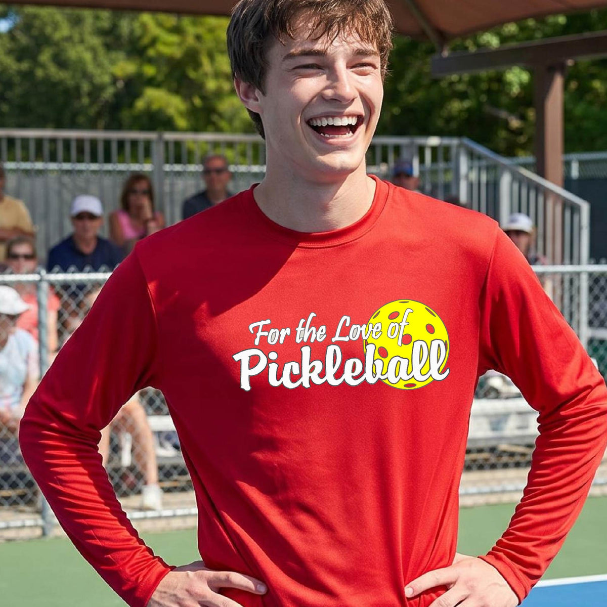 A close-up of a man wearing a red long-sleeve t-shirt with a pickleball graphic on the left bottom left of ‘FOR THE LOVE OF PICKLEBALL’ in white with a yellow pickleball behind it.  