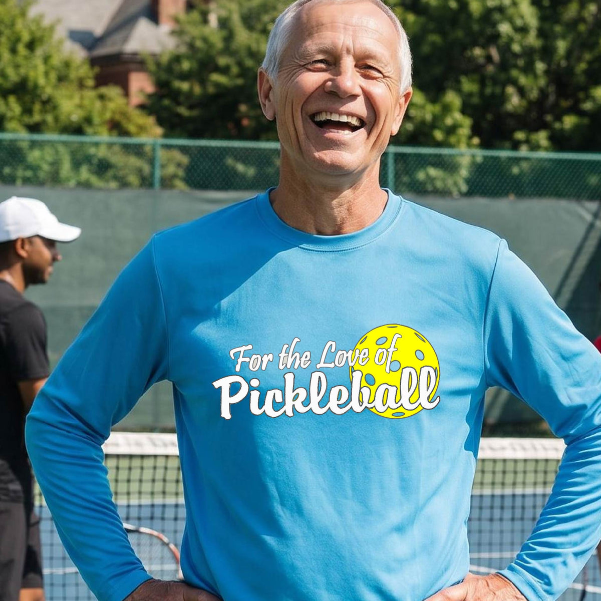 A close-up of a man wearing a bright blue long-sleeve t-shirt with a pickleball graphic on the left bottom left of ‘FOR THE LOVE OF PICKLEBALL’ in white with a yellow pickleball behind it.  