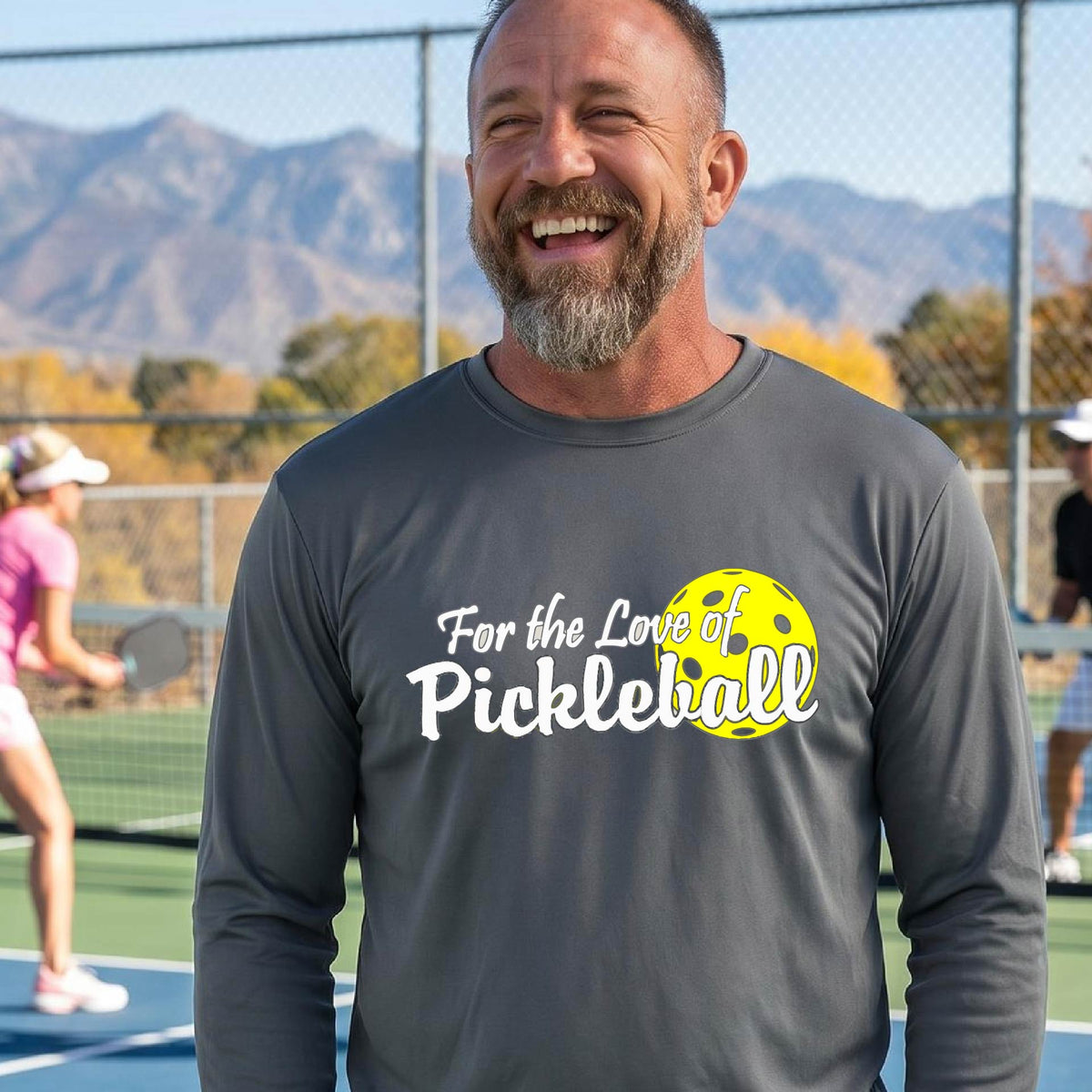 A close-up of a man wearing a gray long-sleeve t-shirt with a pickleball graphic on the left bottom left of ‘FOR THE LOVE OF PICKLEBALL’ in white with a yellow pickleball behind it.  