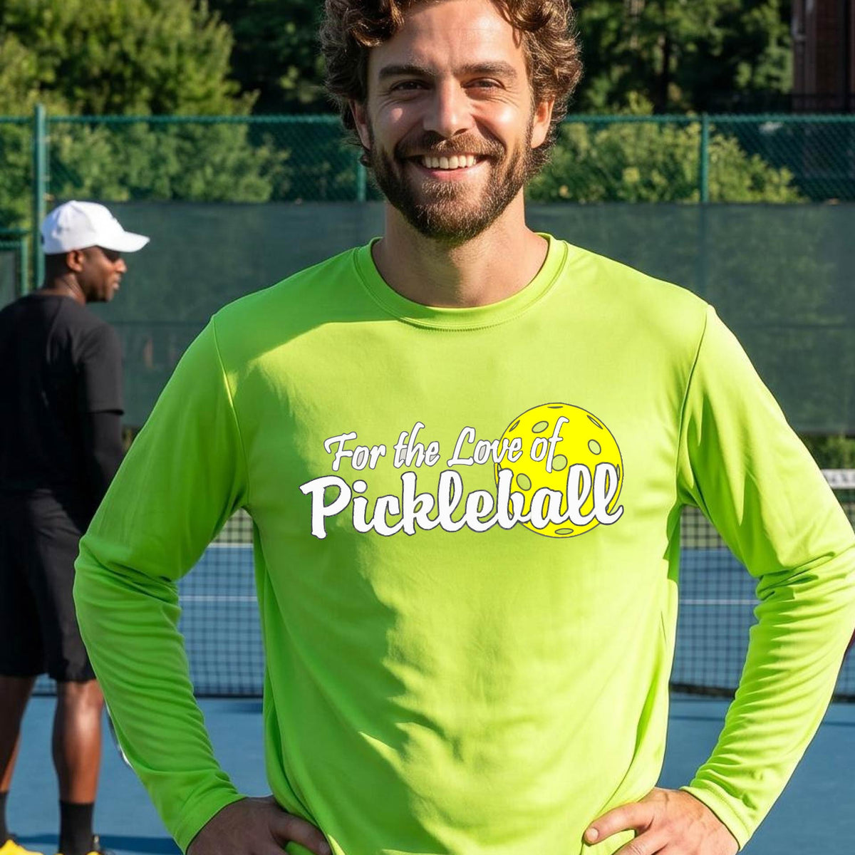 A close-up of a man wearing a lime green long-sleeve t-shirt with a pickleball graphic on the left bottom left of ‘FOR THE LOVE OF PICKLEBALL’ in white with a yellow pickleball behind it.  