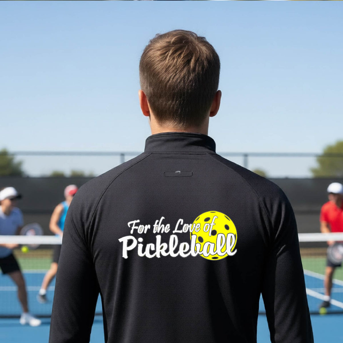 A close-up of a man wearing a black quarter-zip shirt with a pickleball graphic on the left bottom left of ‘FOR THE LOVE OF PICKLEBALL’ in white with a yellow pickleball behind it.  