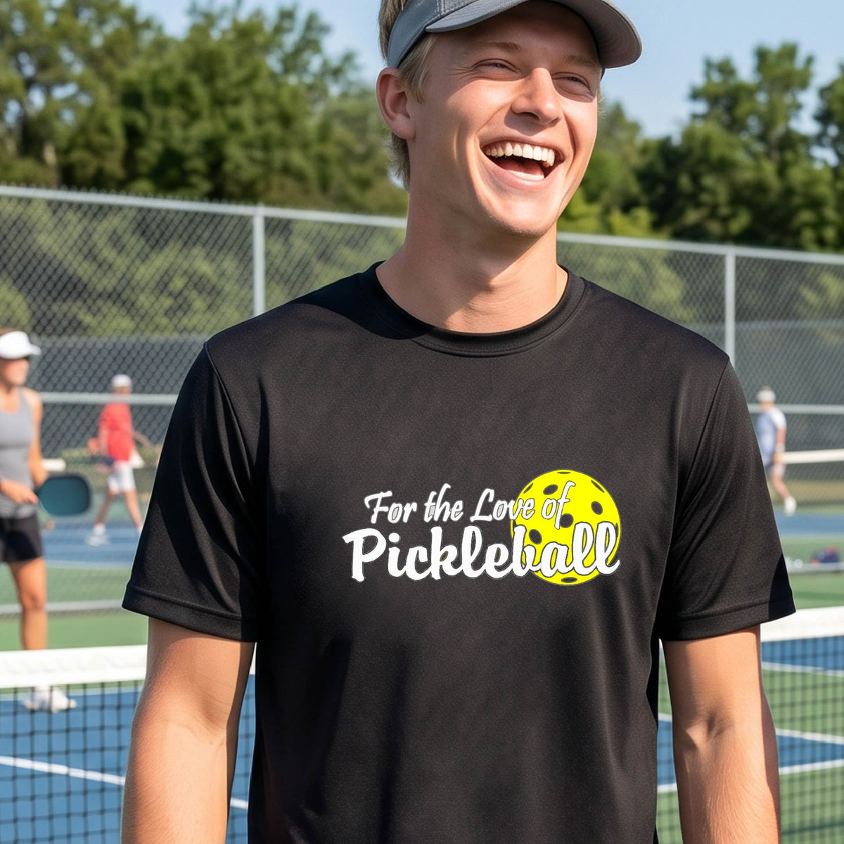 A close-up of a man wearing a black short-sleeve t-shirt with a pickleball graphic on the left bottom left of ‘FOR THE LOVE OF PICKLEBALL’ in white with a yellow pickleball behind it.  