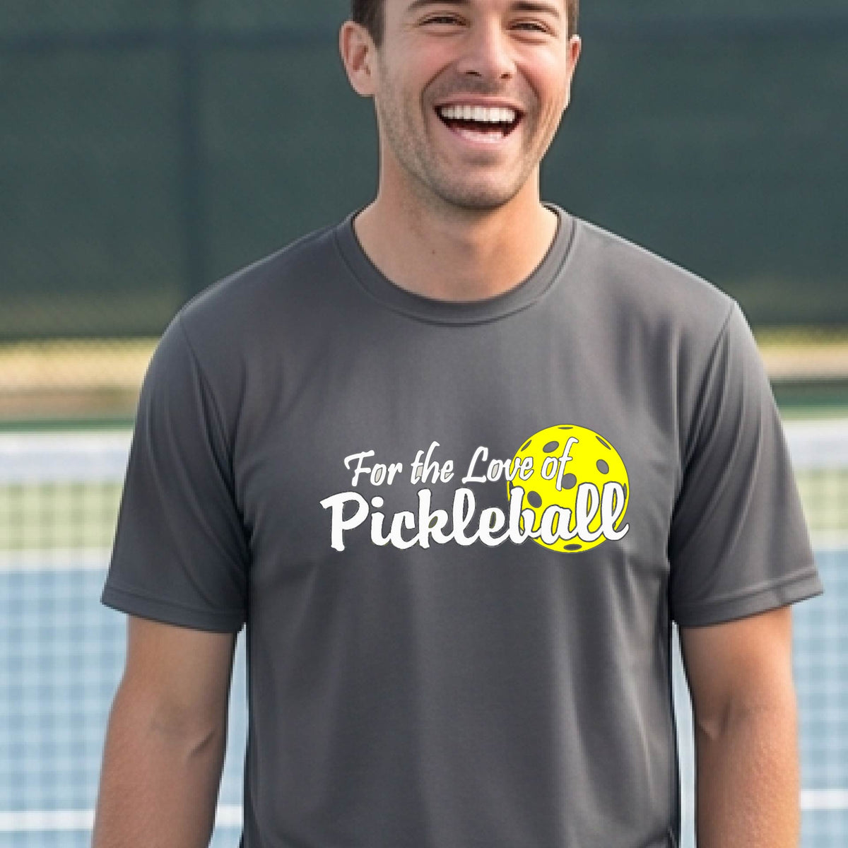 A close-up of a man wearing a gray short-sleeve t-shirt with a pickleball graphic on the left bottom left of ‘FOR THE LOVE OF PICKLEBALL’ in white with a yellow pickleball behind it.  