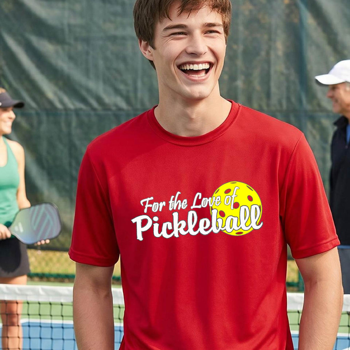 A close-up of a man wearing a red short-sleeve t-shirt with a pickleball graphic on the left bottom left of ‘FOR THE LOVE OF PICKLEBALL’ in white with a yellow pickleball behind it.  