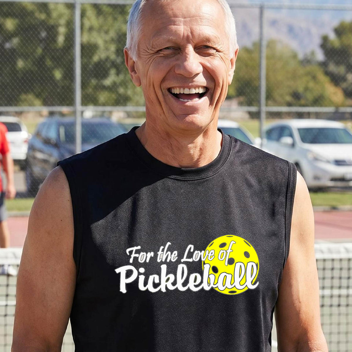 A close-up of a man wearing a black sleeveless t-shirt with a pickleball graphic on the left bottom left of ‘FOR THE LOVE OF PICKLEBALL’ in white with a yellow pickleball behind it.  