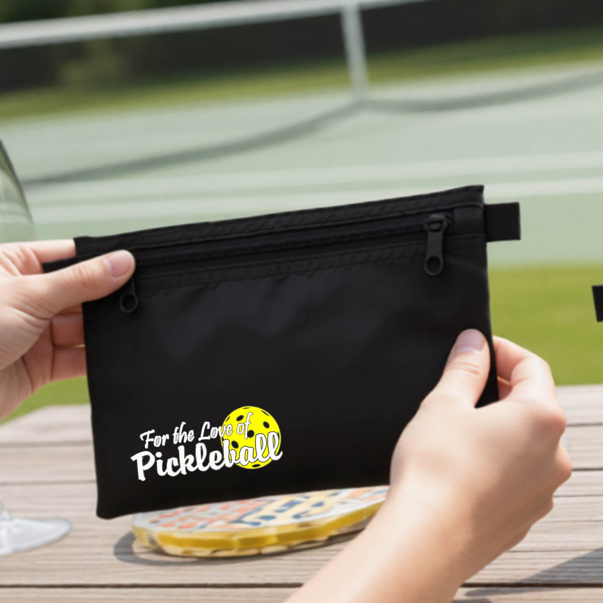 A close-up of a black cosmetic toiletry bag with a pickleball graphic of ‘FOR THE LOVE OF PICKLEBALL’ in white with a yellow pickleball behind it.  
