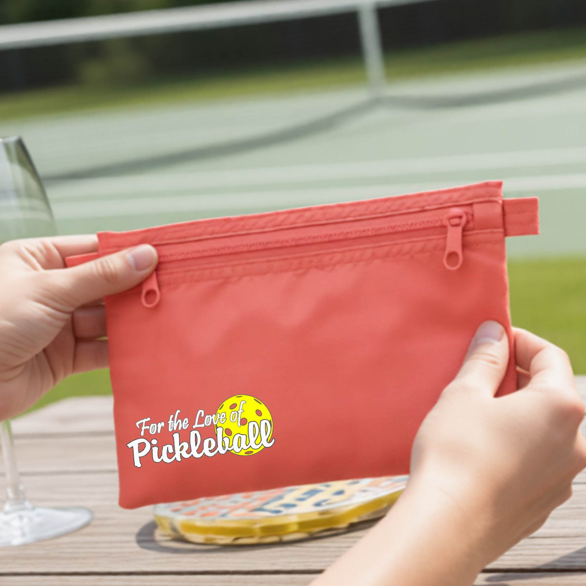 A close-up of a coral cosmetic toiletry bag with a pickleball graphic of ‘FOR THE LOVE OF PICKLEBALL’ in white with a yellow pickleball behind it.  