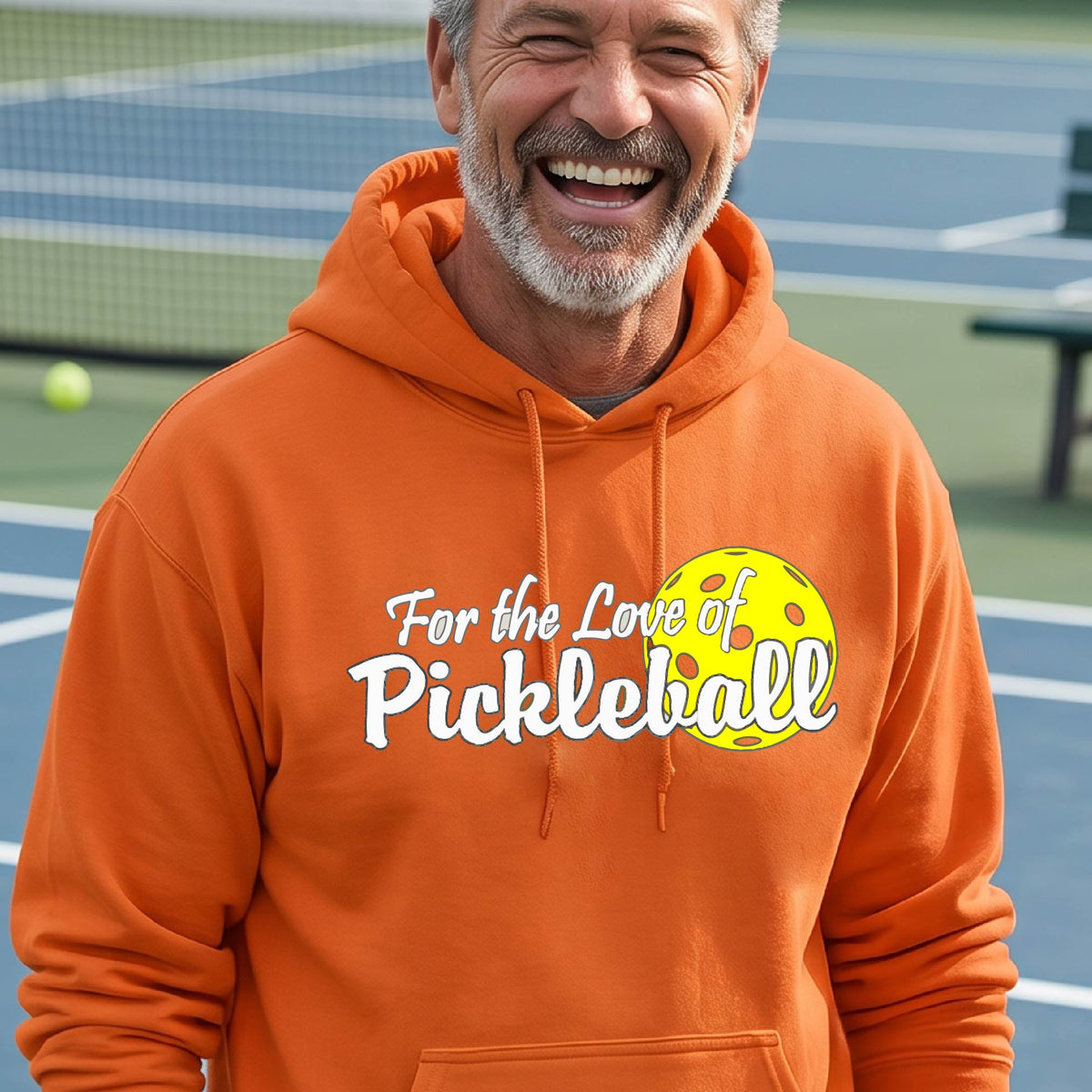 A close-up of an orangeunisex hoodie pullover with a pickleball graphic of ‘FOR THE LOVE OF PICKLEBALL’ in white with a yellow pickleball behind it graphic on the front.