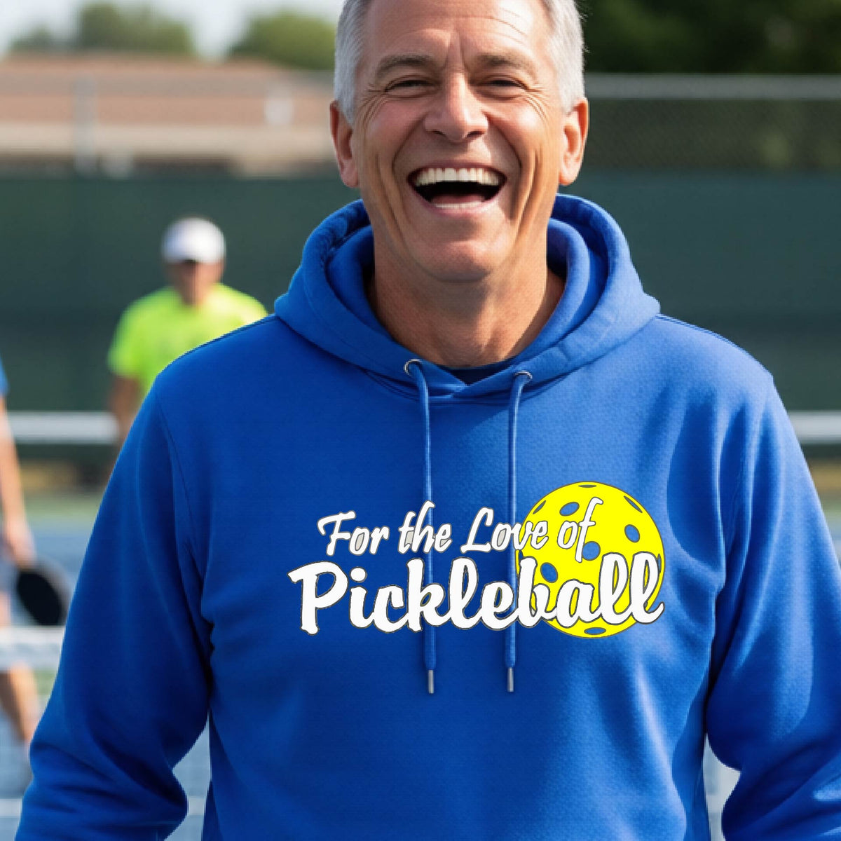 A close-up of a royal blue unisex hoodie pullover with a pickleball graphic of ‘FOR THE LOVE OF PICKLEBALL’ in white with a yellow pickleball behind it graphic on the front.