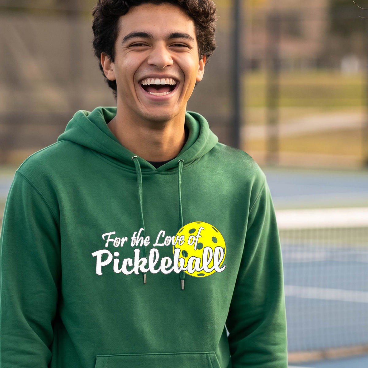 A close-up of a green unisex hoodie pullover with a pickleball graphic of ‘FOR THE LOVE OF PICKLEBALL’ in white with a yellow pickleball behind it graphic on the front.