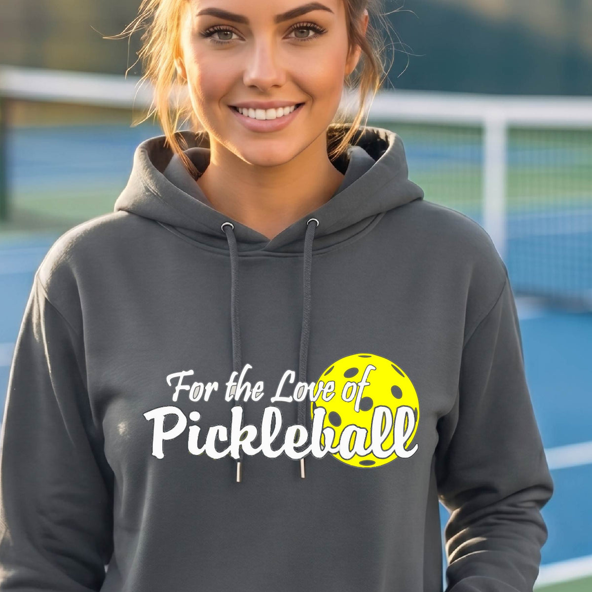 A close-up of a dark gray unisex hoodie pullover with a pickleball graphic of ‘FOR THE LOVE OF PICKLEBALL’ in white with a yellow pickleball behind it graphic on the front.