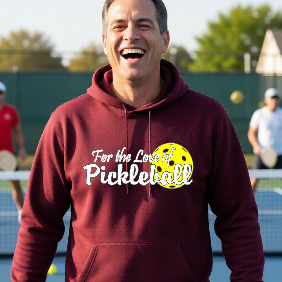 A close-up of a maroon unisex hoodie pullover with a pickleball graphic of ‘FOR THE LOVE OF PICKLEBALL’ in white with a yellow pickleball behind it graphic on the front.