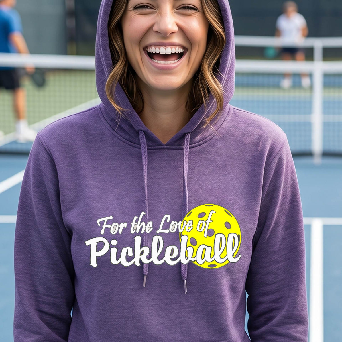 A closeup of a woman wearing a purple hoodie pullover with a pickleball graphic on the left bottom left of ‘FOR THE LOVE OF PICKLEBLL’ in white with a yellow pickleball behind it.  