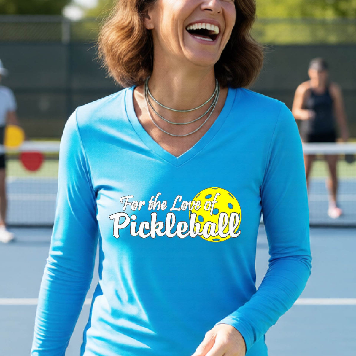 A close-up of a womens bright blue long-sleeve v-neck t-shirt with a pickleball graphic of ‘FOR THE LOVE OF PICKLEBALL’ in white with a yellow pickleball behind it graphic on the front.