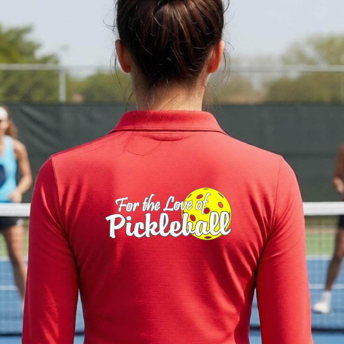 A closeup of a woman wearing a red quarter-zip shirt with a pickleball graphic on the left bottom left of ‘FOR THE LOVE OF PICKLEBLL’ in white with a yellow pickleball behind it.  
