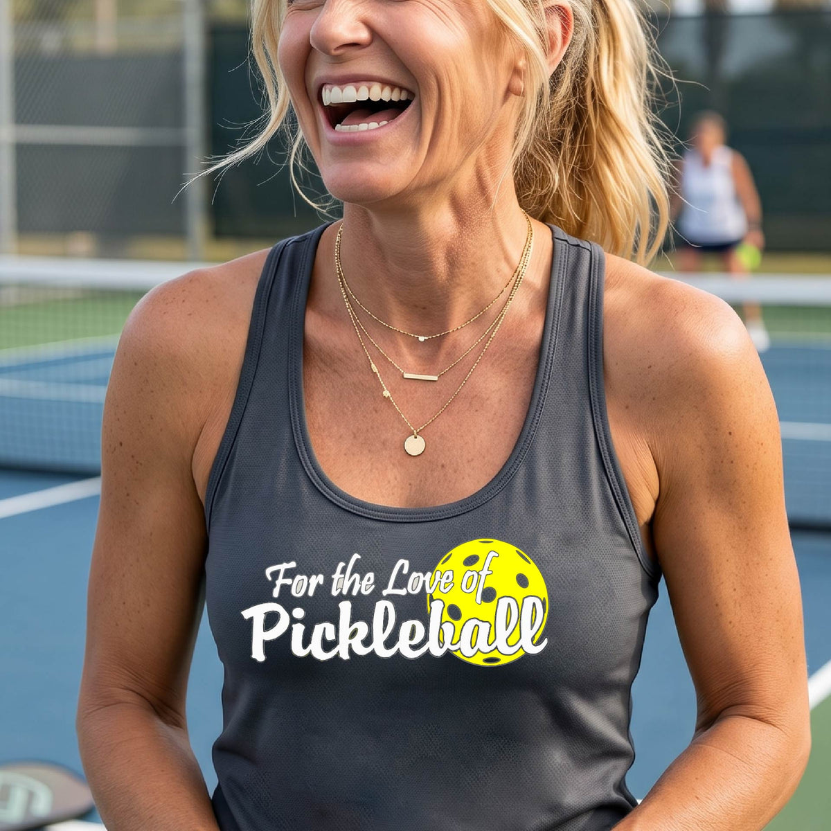 A close-up of a dark gray womens racerback tank with a pickleball graphic of ‘FOR THE LOVE OF PICKLEBALL’ in white with a yellow pickleball behind it graphic on the front.