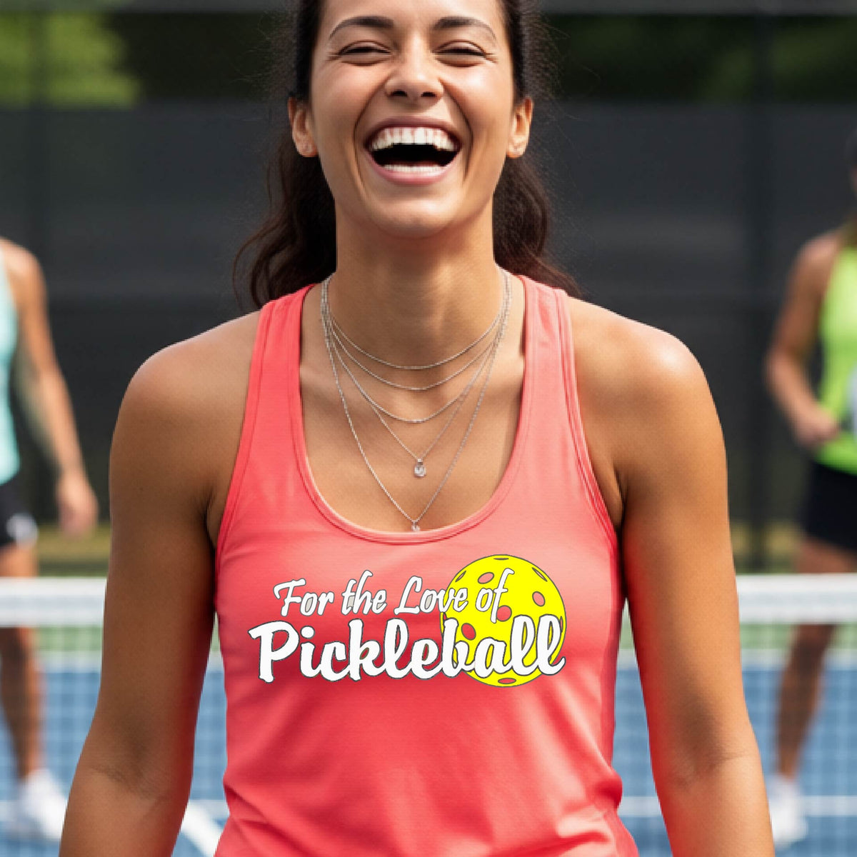 A close-up of a coral pink womens racerback tank with a pickleball graphic of ‘FOR THE LOVE OF PICKLEBALL’ in white with a yellow pickleball behind it graphic on the front.