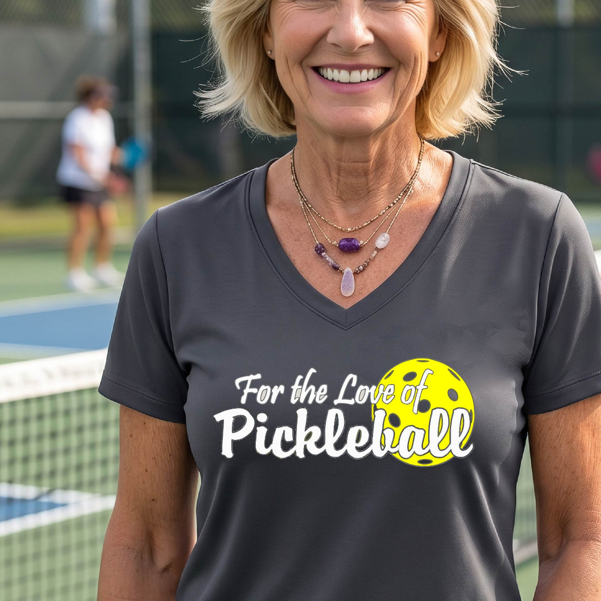 A close-up of a womens dark gray short-sleeve v-neck t-shirt with a pickleball graphic of ‘FOR THE LOVE OF PICKLEBALL’ in white with a yellow pickleball behind it graphic on the front.
