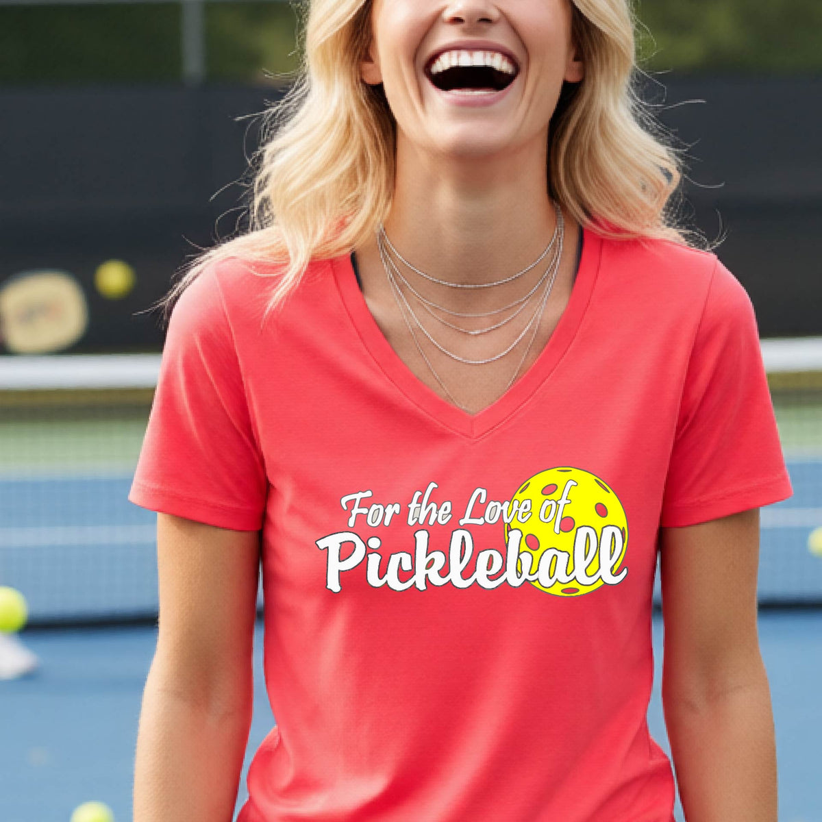 A close-up of a womens coral pink short-sleeve v-neck t-shirt with a pickleball graphic of ‘FOR THE LOVE OF PICKLEBALL’ in white with a yellow pickleball behind it graphic on the front.