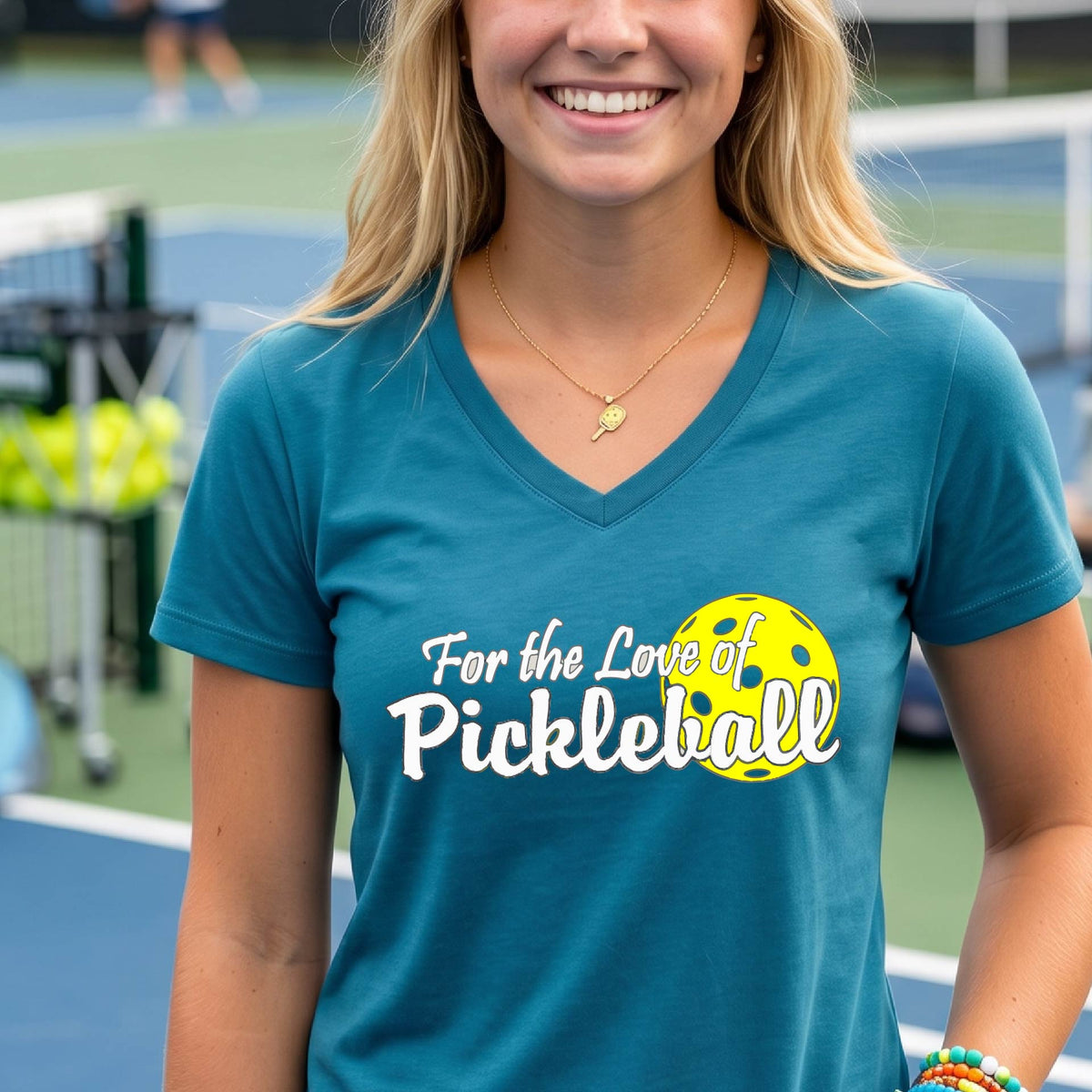 A close-up of a womens teal short-sleeve v-neck t-shirt with a pickleball graphic of ‘FOR THE LOVE OF PICKLEBALL’ in white with a yellow pickleball behind it graphic on the front.