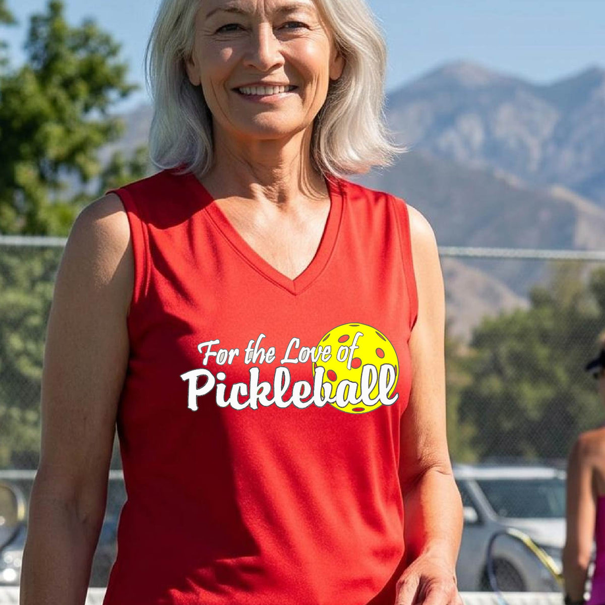 A closeup of a woman wearing a red sleeveless tank top with a pickleball graphic on the left bottom left of ‘FOR THE LOVE OF PICKLEBLL’ in white with a yellow pickleball behind it.  