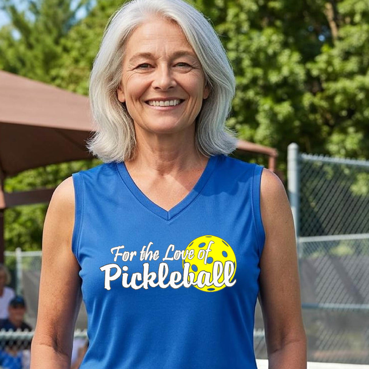 A closeup of a woman wearing a royal blue sleeveless tank top with a pickleball graphic on the left bottom left of ‘FOR THE LOVE OF PICKLEBLL’ in white with a yellow pickleball behind it.  