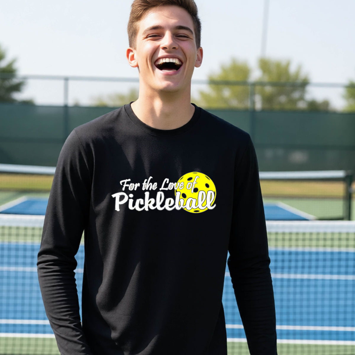 A closeup of a young person wearing a black long-sleeve athletic shirt with a pickleball graphic on the left bottom left of ‘FOR THE LOVE OF PICKLEBLL’ in white with a yellow pickleball behind it.  