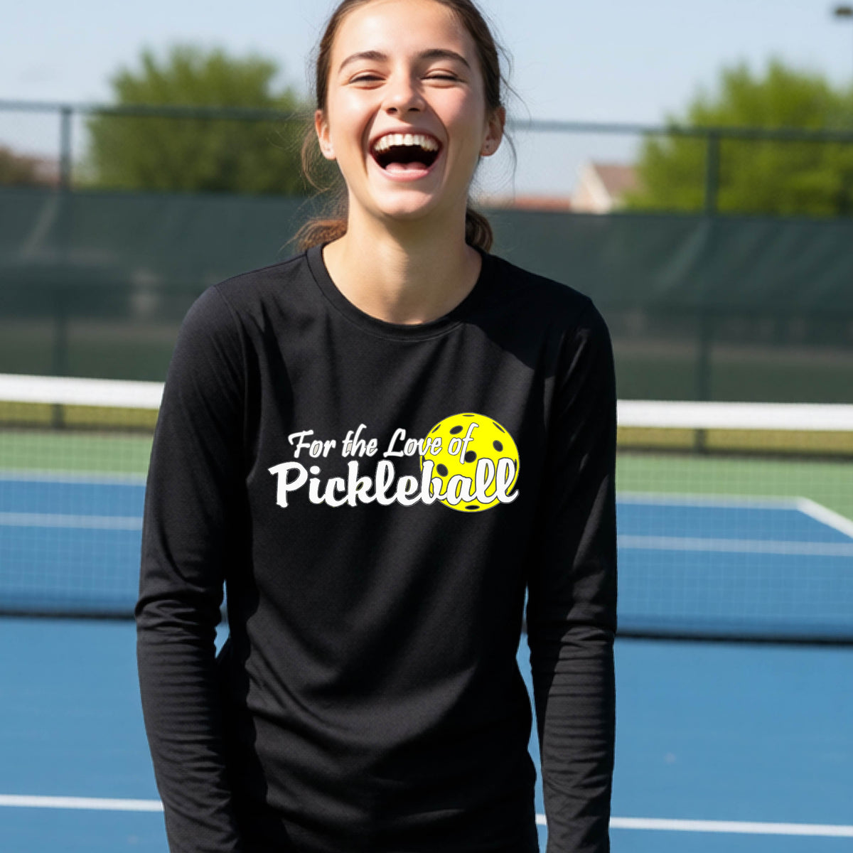 A closeup of a young person wearing a black long-sleeve athletic shirt with a pickleball graphic on the left bottom left of ‘FOR THE LOVE OF PICKLEBLL’ in white with a yellow pickleball behind it.  