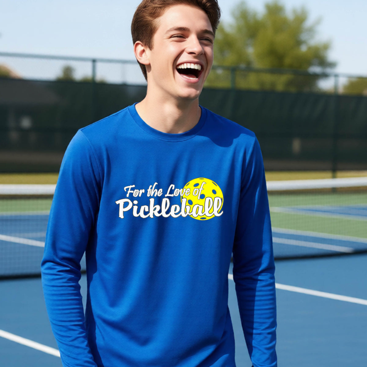 A closeup of a young person wearing a royal long-sleeve athletic shirt with a pickleball graphic on the left bottom left of ‘FOR THE LOVE OF PICKLEBLL’ in white with a yellow pickleball behind it.  
