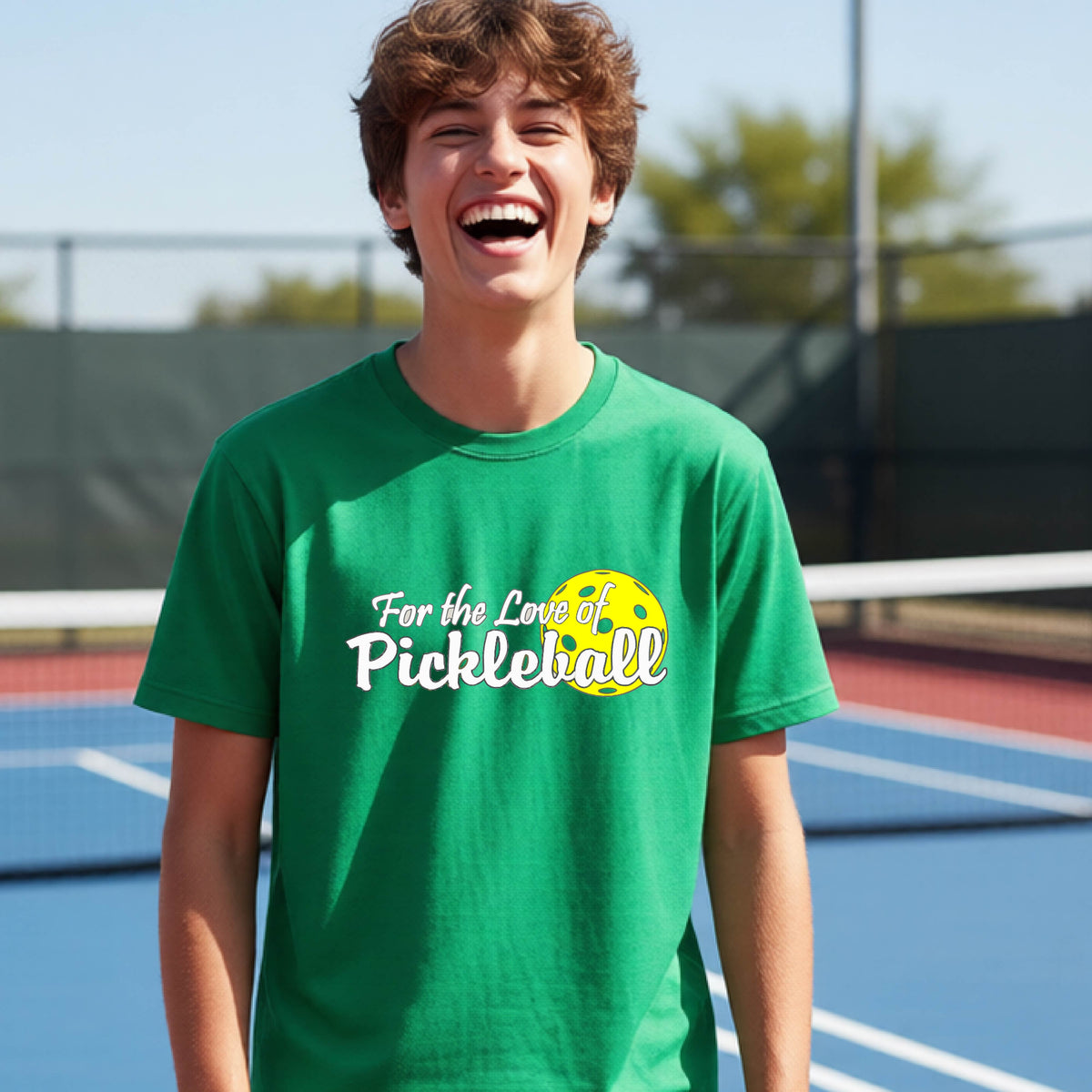 
A closeup of a young person wearing a green short-sleeve athletic shirt with a pickleball graphic on the left bottom left of ‘FOR THE LOVE OF PICKLEBLL’ in white with a yellow pickleball behind it.  
