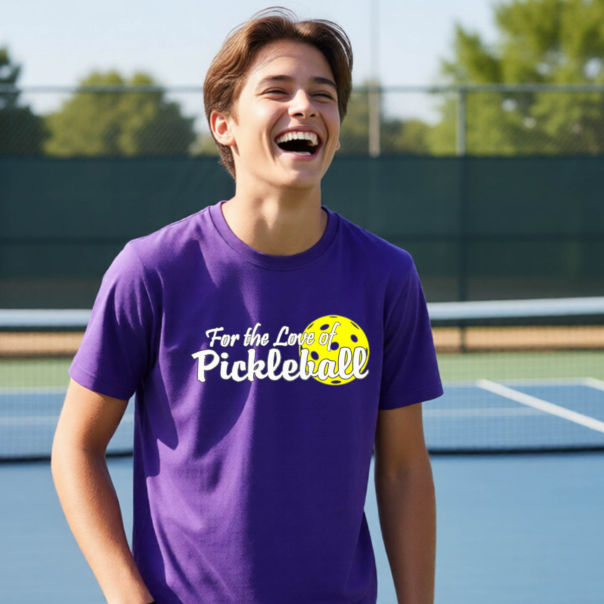 
A closeup of a young person wearing a purple short-sleeve athletic shirt with a pickleball graphic on the left bottom left of ‘FOR THE LOVE OF PICKLEBLL’ in white with a yellow pickleball behind it.  
