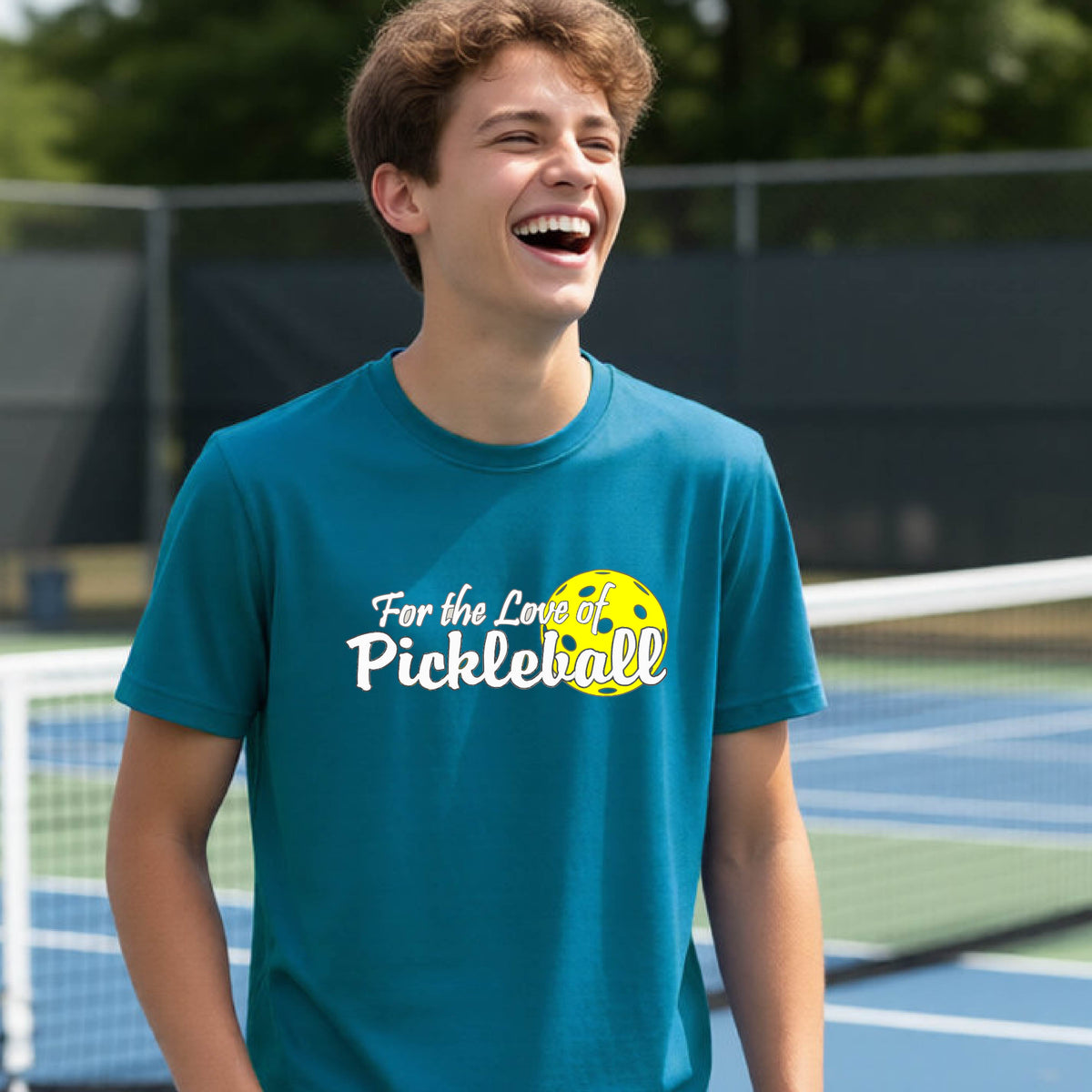 
A closeup of a young person wearing a teal short-sleeve athletic shirt with a pickleball graphic on the left bottom left of ‘FOR THE LOVE OF PICKLEBLL’ in white with a yellow pickleball behind it.  

