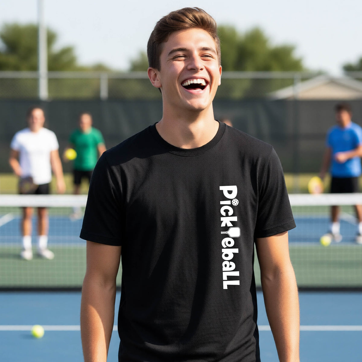 A young person on a pickleball court seen from behind, wearing a black t-shirt with 'Pickleball' printed vertically in white on the front.