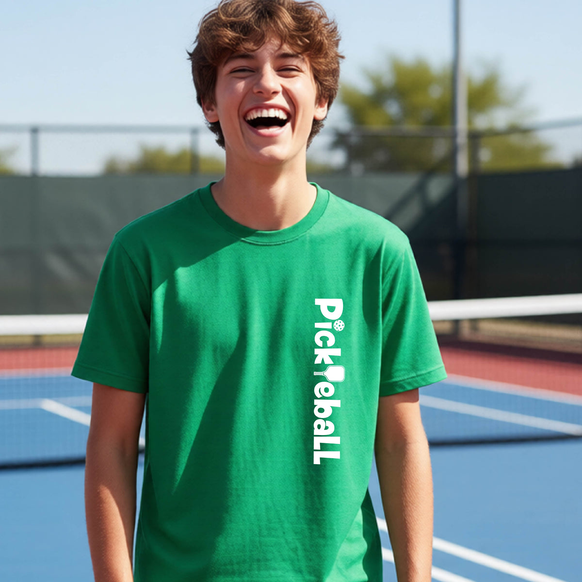 A young person on a pickleball court seen from behind, wearing a green t-shirt with 'Pickleball' printed vertically in white on the front.