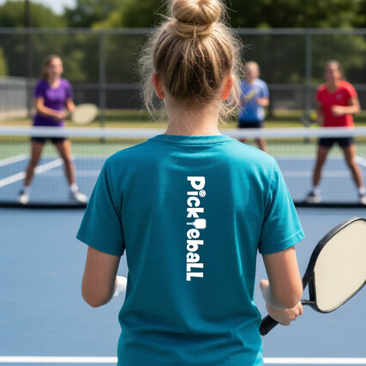 A young person on a pickleball court seen from behind, wearing a teal t-shirt with 'Pickleball' printed vertically in white on the back.